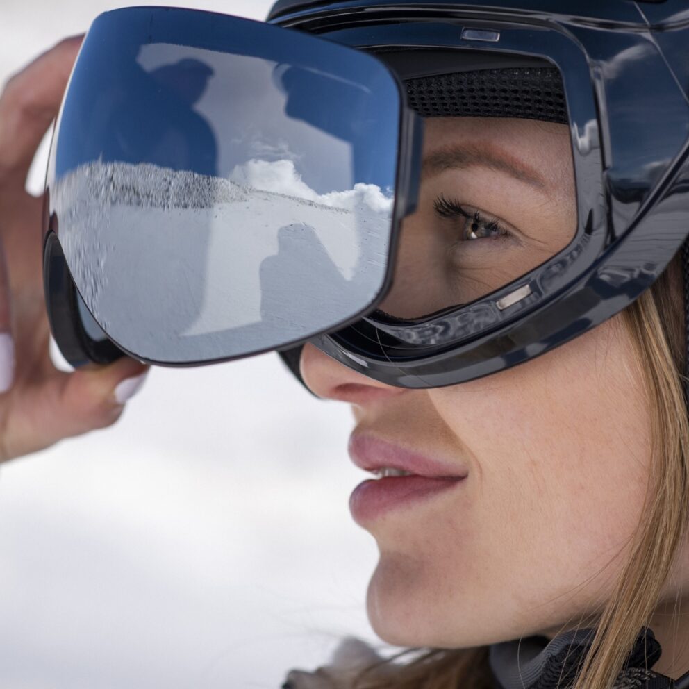 Gros plan sur une skieuse ajustant son masque de ski photochromique DIEZZ avec écran miroir sur fond de neige.